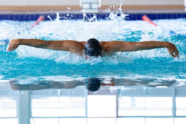 水泳プールでの白人男性水泳のフロントビュー 黒のスイミングキャップとスイミングゴーグル 水泳蝶を身に着けている — ストック写真