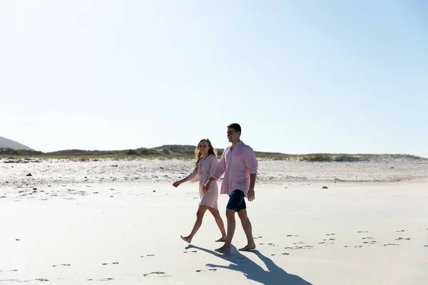 一对白种人夫妇在沙滩上的侧视图 背景是蓝天 他们手牵手散步 — 图库照片