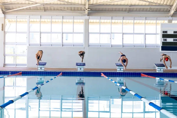 四个男子游泳运动员在游泳池前的景象 从起跳台跳下 跳入水中 游泳运动员为比赛而刻苦训练 — 图库照片