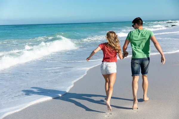 一对白种人夫妇在海滩上的后视镜 背景是蓝天和大海 他们正在奔跑 — 图库照片