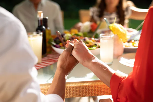 夕食のテーブルセットで家族と一緒に外に座っている白人のカップルの後部ビューミッドセクションでは 祈りの中で手を携えて — ストック写真