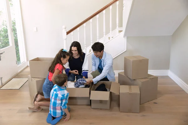 白种人父母带着儿子和女儿打开盒子坐在新家地板上的镜头 — 图库照片