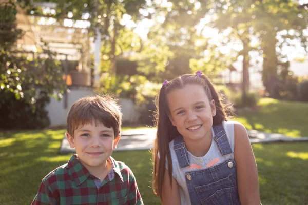 在一个阳光灿烂的花园里 一个有着棕色头发和蓝眼睛的白人弟弟和妹妹的画像 两个人都在镜头前笑着 — 图库照片
