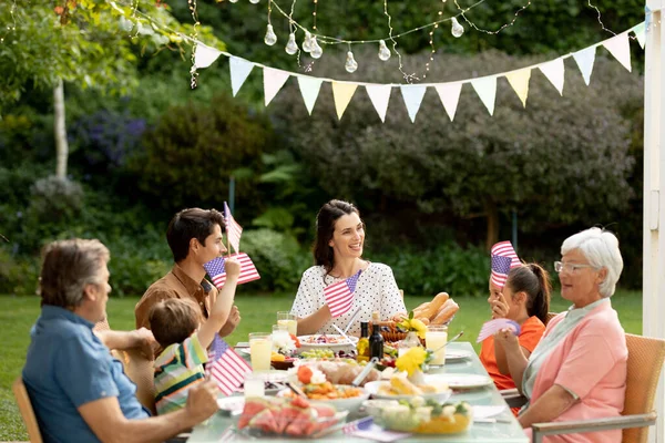 一个多代白人家庭坐在外面的餐桌前吃饭 庆祝和挥动着我们的国旗 — 图库照片