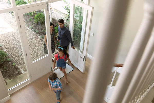 彼らの新しい家の正面玄関に入る白人夫婦と彼らの若い息子と娘の高い角度のビュー 先に実行されている子供たち バニスターを通して見られます — ストック写真