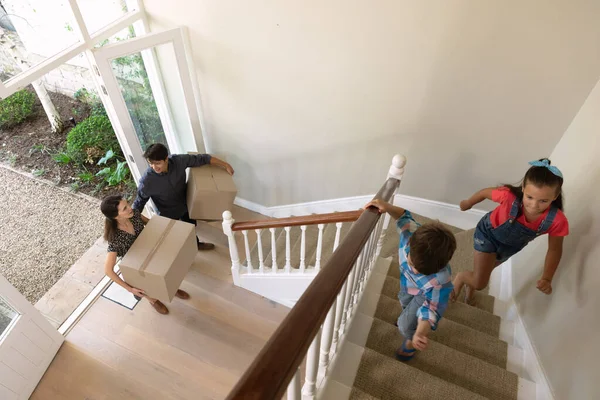 彼らの子供たちが彼らの前の階段を駆け上がる間 彼らの若い息子と娘と一緒に彼らの新しい家に到着し 段ボール箱を移動し 運ぶ白人のカップルの高い角度のビュー — ストック写真