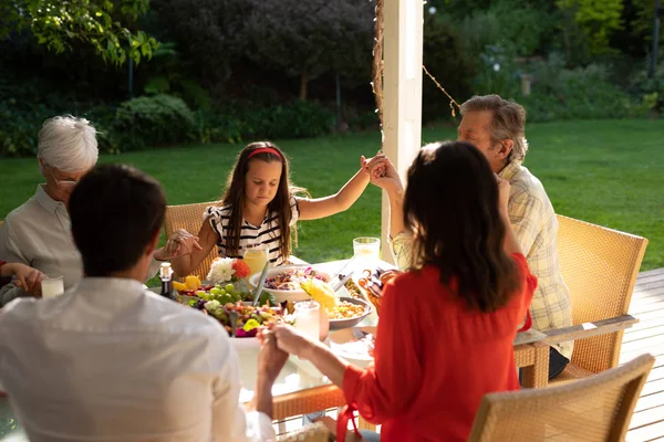 一个多代白人家庭坐在外面餐桌边吃饭 闭着眼睛 手牵手祈祷的高视角画面 — 图库照片