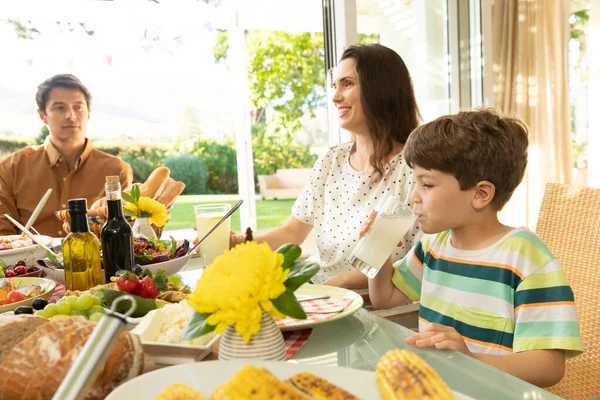 白人のカップルと彼らの若い息子の側面図夕食のテーブルセットの外に座って食事 息子を飲む — ストック写真