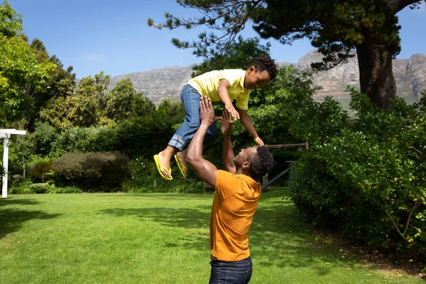 一个在花园里笑着的非裔美国人把他的儿子抛到空中抓住了他 — 图库照片