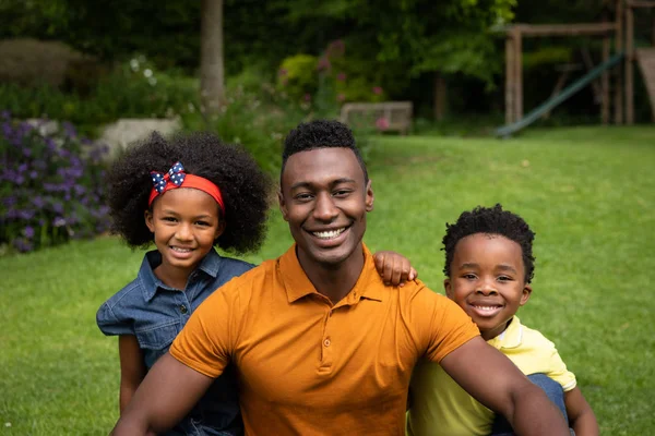一个微笑的非裔美国人和他的女儿和儿子在花园里看着相机的画像 — 图库照片