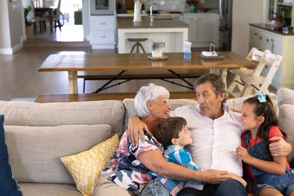 幼い孫と孫が抱き合って笑顔でソファに座っている白人祖父母の正面図 — ストック写真