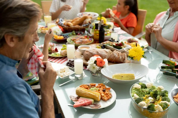 一个多代白人家庭坐在外面餐桌边吃饭的侧视图 — 图库照片