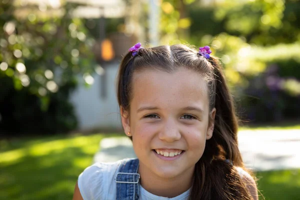 在一个阳光灿烂的花园里 一个有着一头棕色长发和一双蓝眼睛的年轻白人女孩的画像在镜头前微笑着 — 图库照片