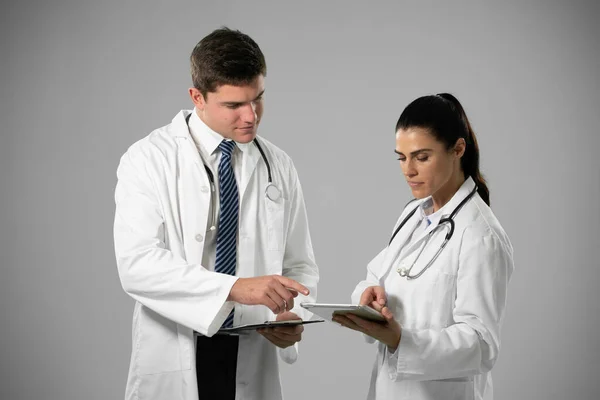 聴診器付きのラボコートを着た白人女性と男性医師の横顔 灰色の背景にデジタルタブレットを使用してクリップボード作成ノートを保持 — ストック写真