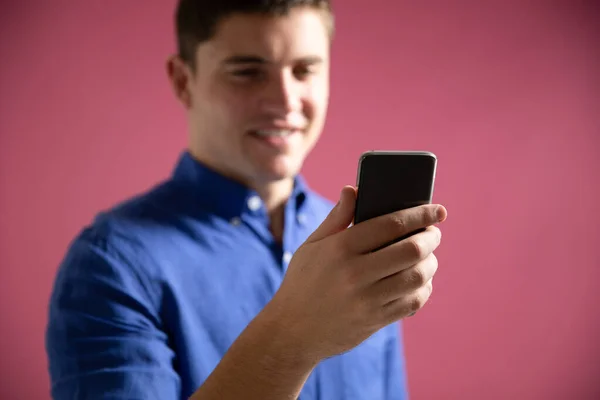 一个快乐的职业白种人穿着蓝色的衬衫在办公室工作 站在那里 用智能手机在粉色背景下微笑 他的低视角正面形象 — 图库照片