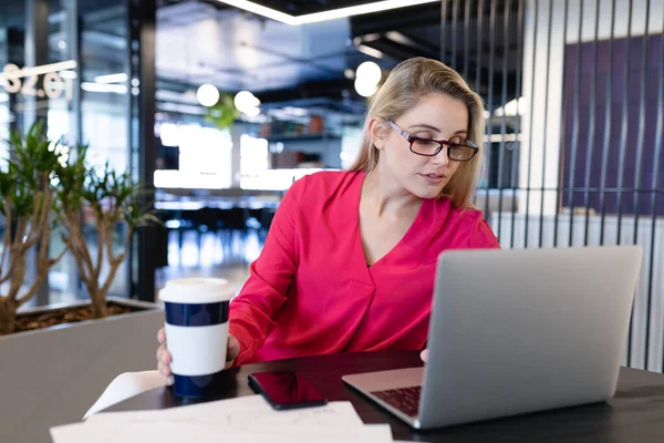 現代のオフィスで机のそばに座りノートパソコンを使っている白人の実業家の女性の正面図 — ストック写真