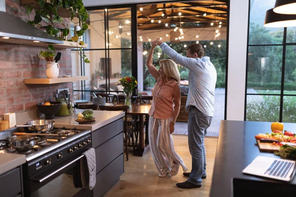 Senior Caucasian couple enjoying their time at home together, dancing in a kitchen and smiling, social distancing and self isolation in quarantine lockdown during coronavirus covid19 epidemic