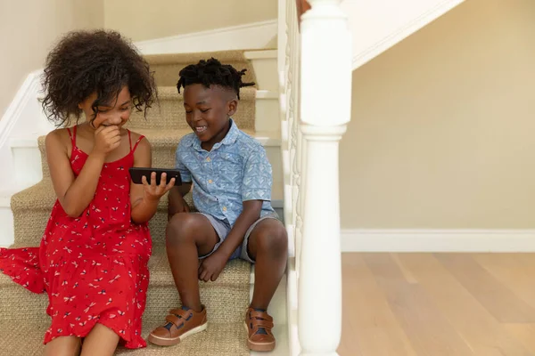 隔离隔离中的自我隔离 一个混血儿和她的弟弟在家里 坐在楼梯上一起看智能手机 — 图库照片