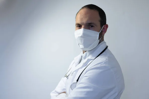 一个身穿医生制服 肩上戴听诊器 戴着面具 站在一间空旷的白色房间里的白人男子的画像 — 图库照片