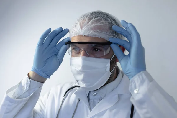 身穿医生制服 肩上戴听诊器的白人男子 戴着面具 站在一间空荡荡的白色房间里 戴着护目镜和手套 — 图库照片