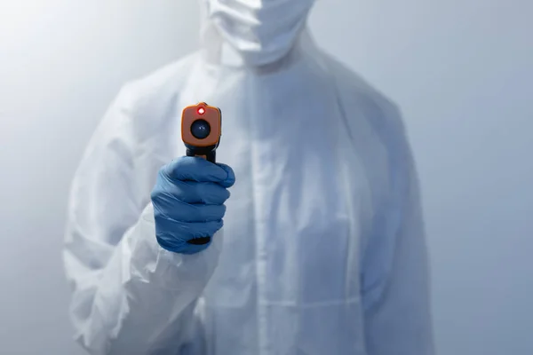 身穿实验室工作服 戴着面罩 戴着手套的妇女中间 站在一个空的白色房间里 用温度计测量温度 — 图库照片