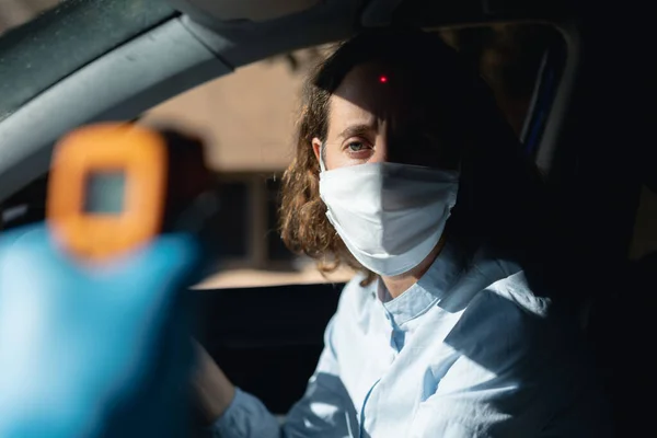 一个男人的手拿着一个白人女人的体温坐在她的车里 戴着面具 — 图库照片