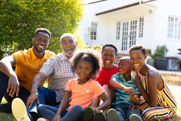 Three generation African American family spending time in their garden on a sunny day, smiling and looking straight into a camera.