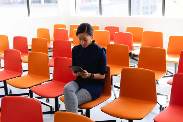 一个身穿漂亮衣服的混血女商人坐在一间空荡荡的现代化会议室里用平板电脑 — 图库照片