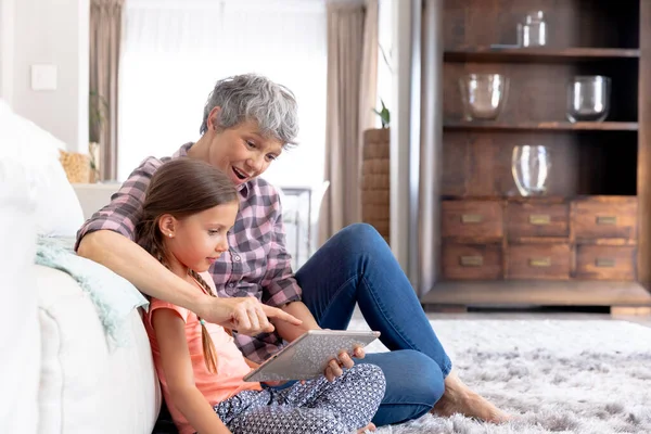 高个子白人妇女和孙女一起呆在家里 坐在客厅的沙发上 用平板电脑 — 图库照片