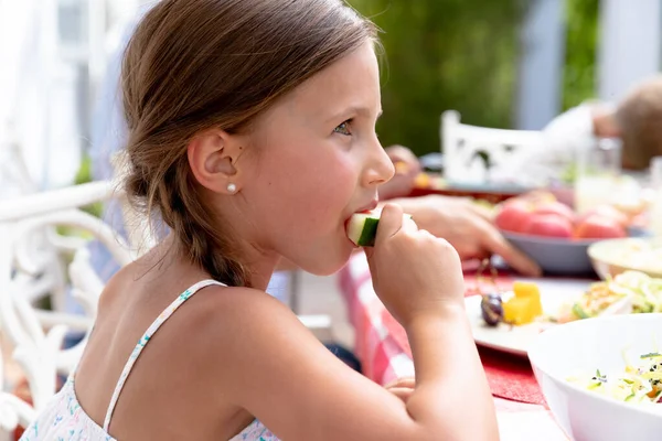 晴れた日に庭のテーブルに座っている白人の女の子と家族の昼食中にスイカのスライスを食べる — ストック写真