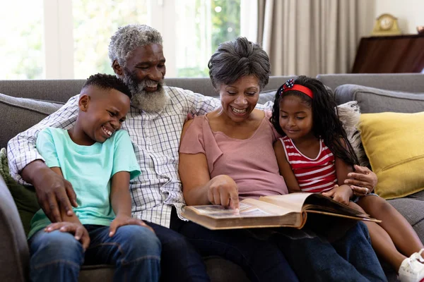 上了年纪的混血种族夫妇和他们的孙子孙女在一起 享受他们在家里的时光 坐在沙发上 — 图库照片