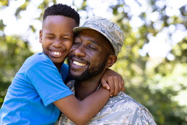 アフリカ系アメリカ人の男は 軍の制服を着て 家に戻り 息子を抱きかかえ 目を閉じて笑顔で 晴れた日に — ストック写真