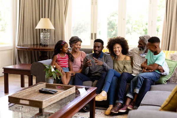 代代相传的混血种族家庭享受着在家里呆在一起的时光 坐在沙发上 彼此交谈 相互凝视 面带微笑 — 图库照片