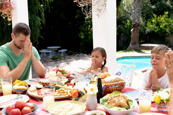 在阳光明媚的日子 白种人三代一家人在花园里共进午餐 坐在桌旁祈祷 — 图库照片