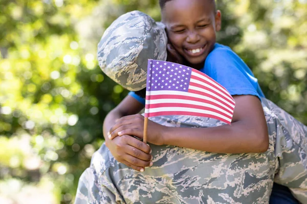 아프리카 미국인 군복을 집으로 돌아오고 아들을 포옹하고 카메라를 웃으며 깃발을 — 스톡 사진