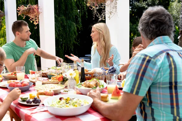 在阳光明媚的日子 白种人三代一家人在花园里吃午饭 坐在一张桌子旁 互相交流 — 图库照片