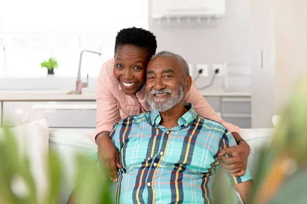 Pareja Afroamericana Mayor Pasando Tiempo Casa Abrazando Sonriendo Mirando Directamente —  Fotos de Stock