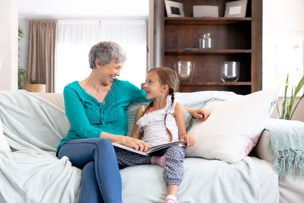 シニア白人女性過ごす時間とともに自宅で彼女の孫娘とともに長い組紐 ソファに座って 家族のアルバムを見て — ストック写真