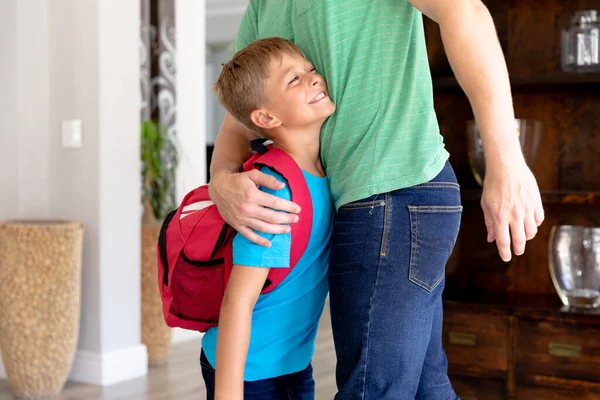 緑色のTシャツを着た白人男性の真ん中のセクションでは 息子が学校を出て抱擁する準備をしている赤いリュックサックを身に着けているのを助けます — ストック写真