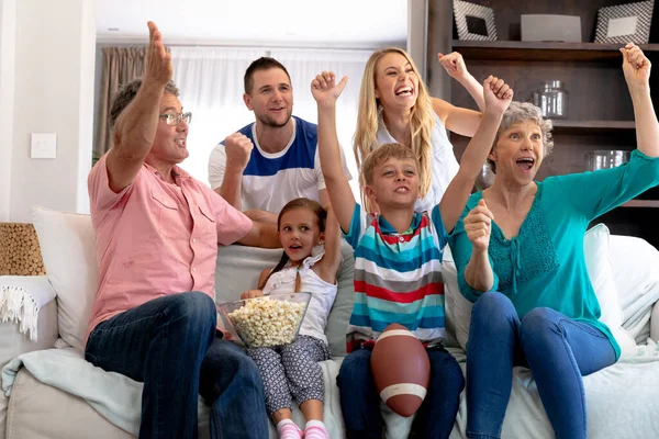 가족은 집에서 시간을 보내고 소파에 앉아서 텔레비전을 즐겁게 환호하고 — 스톡 사진