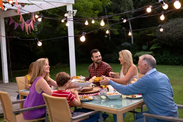 夕食のテーブルセットで外の多世代の白人家族の側面図食事 座って話をし お互いに食べ物を提供する — ストック写真
