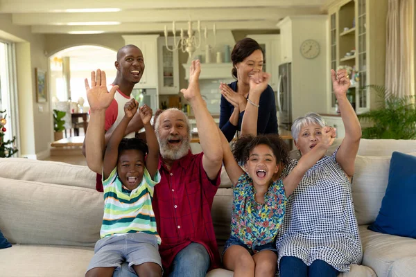 リビングルームの自宅にいる多世代混合人種の家族の肖像画は カメラの笑顔を見て 空中で手を振ってソファに集まりました — ストック写真