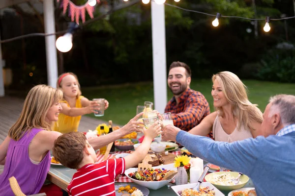 一个多代白人家庭在外面的餐桌边吃饭 举杯举杯敬酒的侧景 — 图库照片