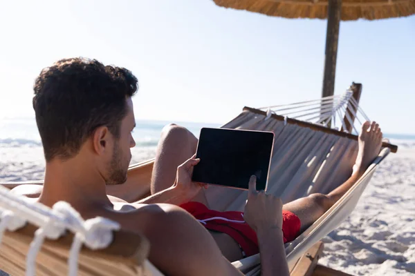 白种人在海滩上享受时光 躺在吊床上 用数字平板电脑 — 图库照片