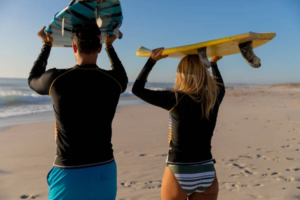 白种人夫妇在海滩上享受时光 头顶着冲浪板 走向大海 — 图库照片