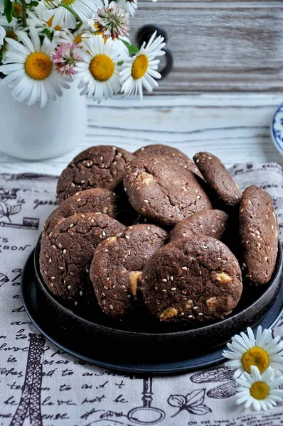 Cookies with cocoa, white chocolate and fried sesame seeds. Background chamomiles