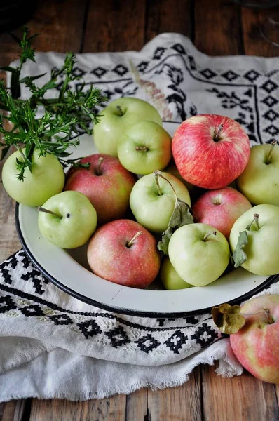 On a wooden table on a cotton towel a metal dish with fresh red and green apples