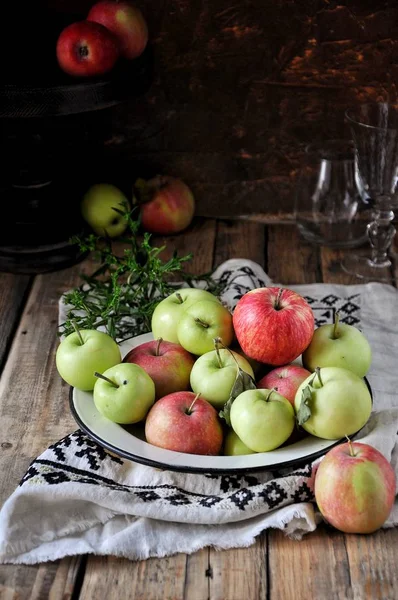 On a wooden table on a cotton towel a metal dish with fresh red and green apples