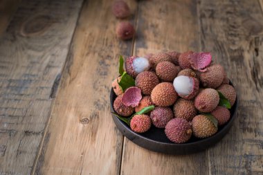 Ahşap arka plan üzerinde siyah bir tabak taze lychee meyvelerin natürmort. Rustik tarzı