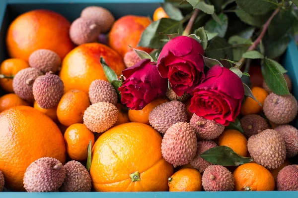 Gift set for the girl. A box of fresh fruit with red oranges, mini tangerines, lychee fruits and red roses